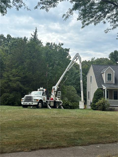 Bucket truck set up beside a home with tall pines